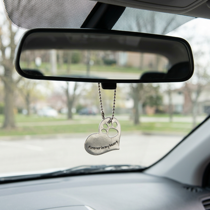 Small pet memorial heart hanging by ball chain beneath a rearview mirror in a parked car
